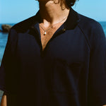 Close up image of male model wearing the navy 'Tompolo'. The image is cropped and shows the model wearing the snaps open, showing off his chain necklace with a drop pearl in the middle. 