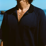 Close up image of male model wearing the navy 'Tompolo'. The image is cropped and shows the model wearing the snaps open, showing off his chain necklace with a drop pearl in the middle. 