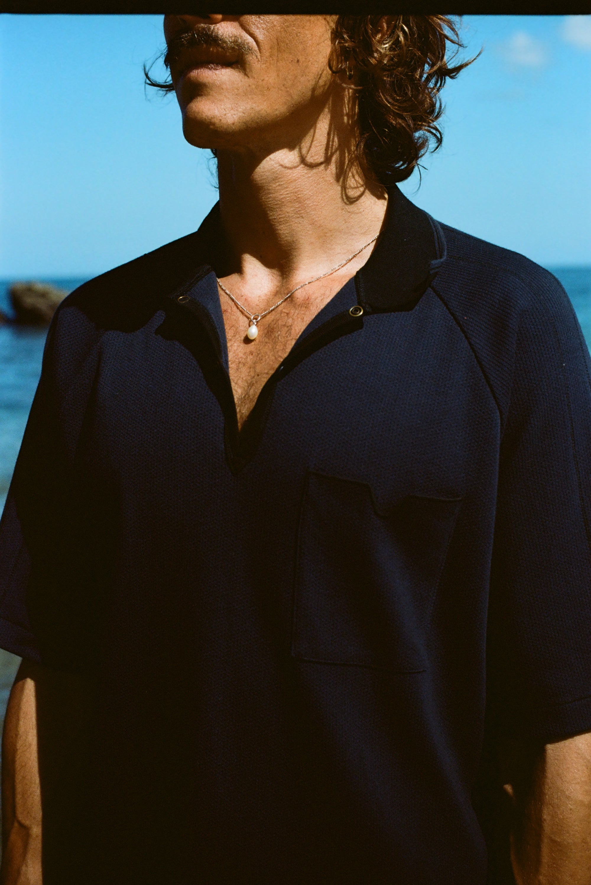 Close up image of male model wearing the navy 'Tompolo'. The image is cropped and shows the model wearing the snaps open, showing off his chain necklace with a drop pearl in the middle. 