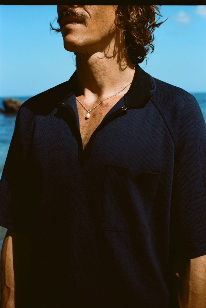Close up image of male model wearing the navy 'Tompolo'. The image is cropped and shows the model wearing the snaps open, showing off his chain necklace with a drop pearl in the middle. 