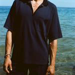 Cropped image of man wearing navy 'TomPolo' with our navy Cabrisa shorts, standing ankle deep in the ocean.