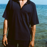 Cropped image of man wearing navy 'TomPolo' with our navy Cabrisa shorts, standing ankle deep in the ocean.