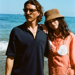 Man and woman posing on the beach wearing the navy mesh 'TomPolo' and our Starfish Strut Shirt in orange. 