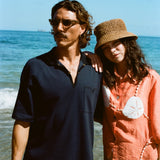 Man and woman posing on the beach wearing the navy mesh 'TomPolo' and our Starfish Strut Shirt in orange. 