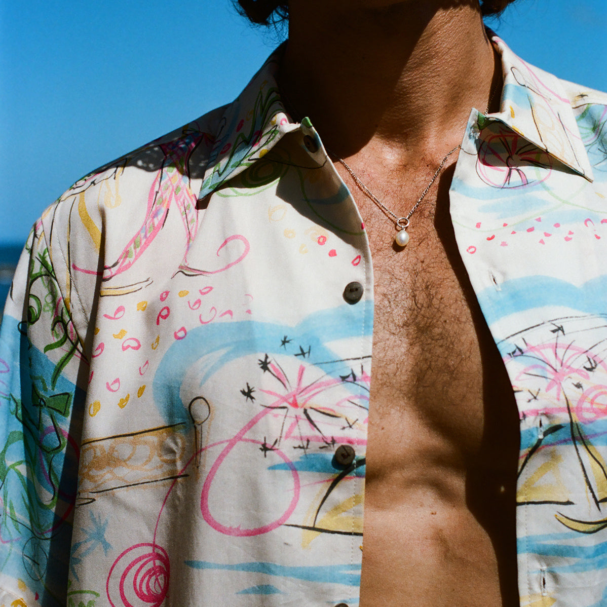 Close-up of a person wearing an open, colorful button-down shirt with abstract pink, blue, and yellow line art.