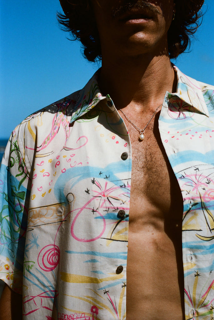 Close-up of a person wearing an open, colorful button-down shirt with abstract pink, blue, and yellow line art.