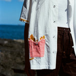 Close-up of a white short-sleeve shirt featuring a red gingham pocket embroidered with golden French fries, worn with brown drawstring shorts.