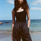 Woman standing on beach, wearing the Easy Going Shorts in Navy Jacquard, with a blank tank top, and one hand in her pocket.