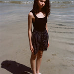 Woman standing on beach, wearing the Easy Going Shorts in Navy Jacquard, with a blank tank top and white sandals. 