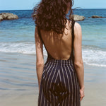 Woman standing on a beach with her back to us. She is wearing a black tank top and our Navy Easy Going Shorts with beige stripes. 
