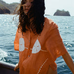 Image of brunette woman wearing the coral 'Sand Dollar Stimulus' ~ Relaxed Crop Cut, sitting on a boat and looking off to the side, with her hair blowing in the wind.