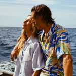 Male model wearing our 'Perfect Cast' Shirt, with his arm around a female model wearing the light blue sand dollar bikini shirt. Both are smiling while riding a boat.