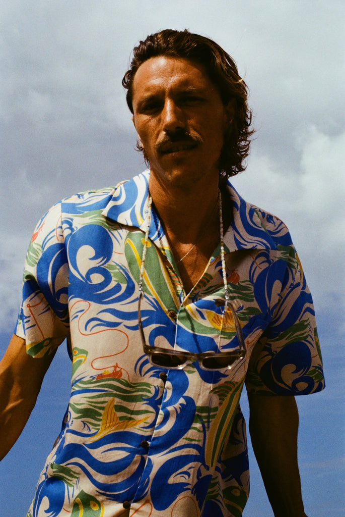 The same male model with longer hair and a mustache is staring into the camera, wearing our patterned 'Perfect Cast' Shirt and a pair of sunglasses are strapped around his neck. 
