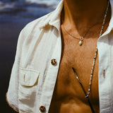Close up of a man's chest, wearing a white shirt open, a necklace with a pearl and sunglasses with a beaded sunglasses chain