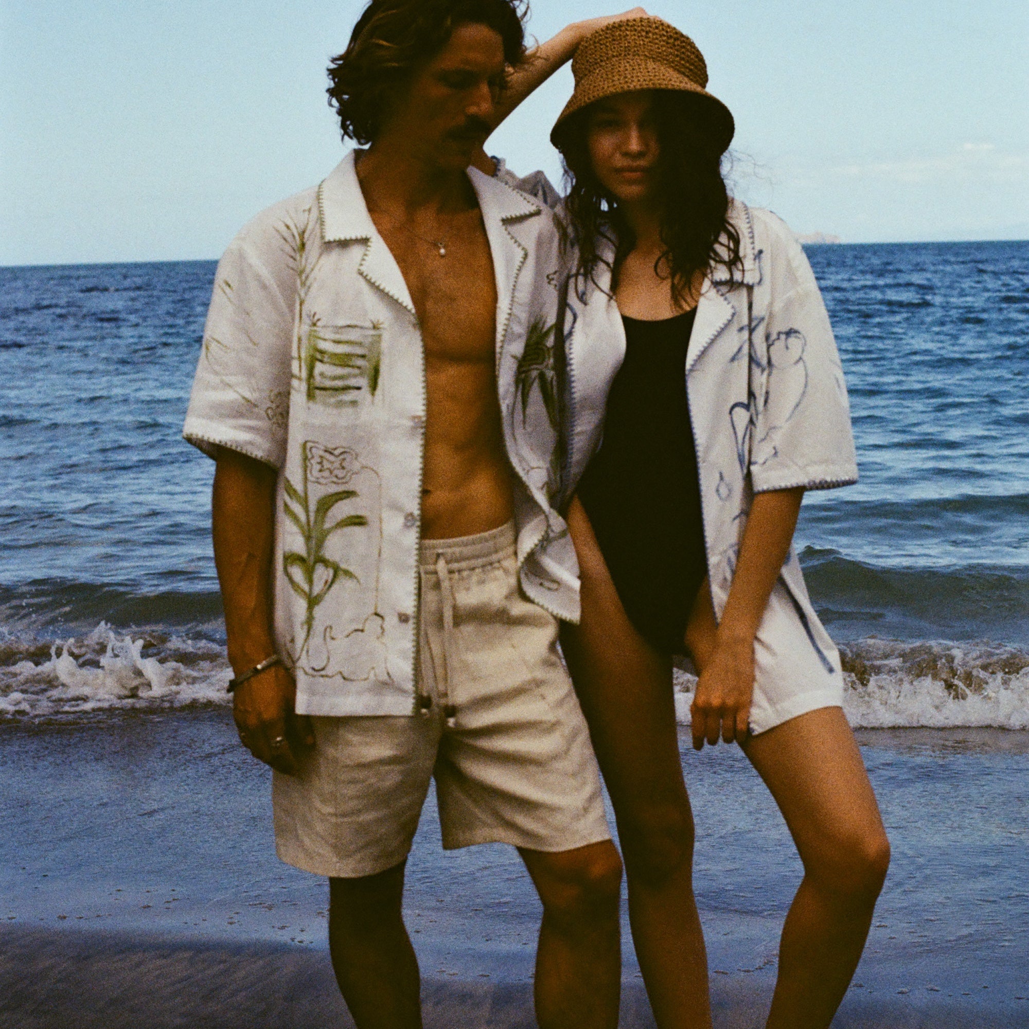 Man and woman standing close together on a beach, both wearing the 'Seasons of Change' by Mary Ball Shirts opened.