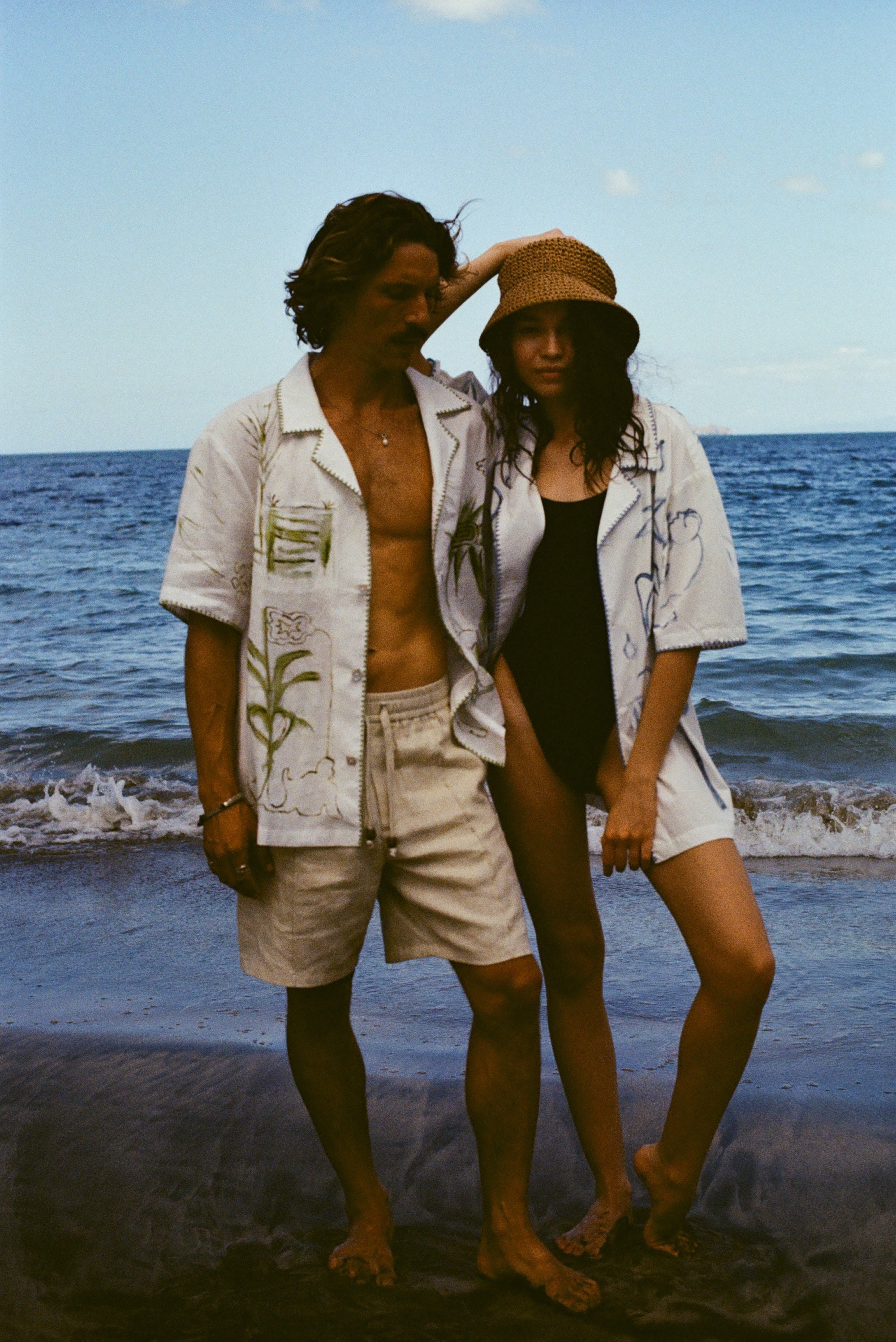 Man and woman standing close together on a beach, both wearing the 'Seasons of Change' by Mary Ball Shirts opened.