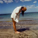 Woman on beach standing with her side to us, wearing the 'Seasons of Change' by Mary Ball Shirt and looking down into the sand. 