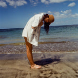 Woman on beach standing with her side to us, wearing the 'Seasons of Change' by Mary Ball Shirt and looking down into the sand. 