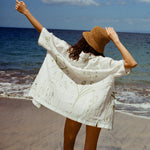 Woman standing on beach facing the ocean with her back to us, while wearing the 'Seasons of Change' by Mary Ball Shirt in Green. Her arms are up in the air. 