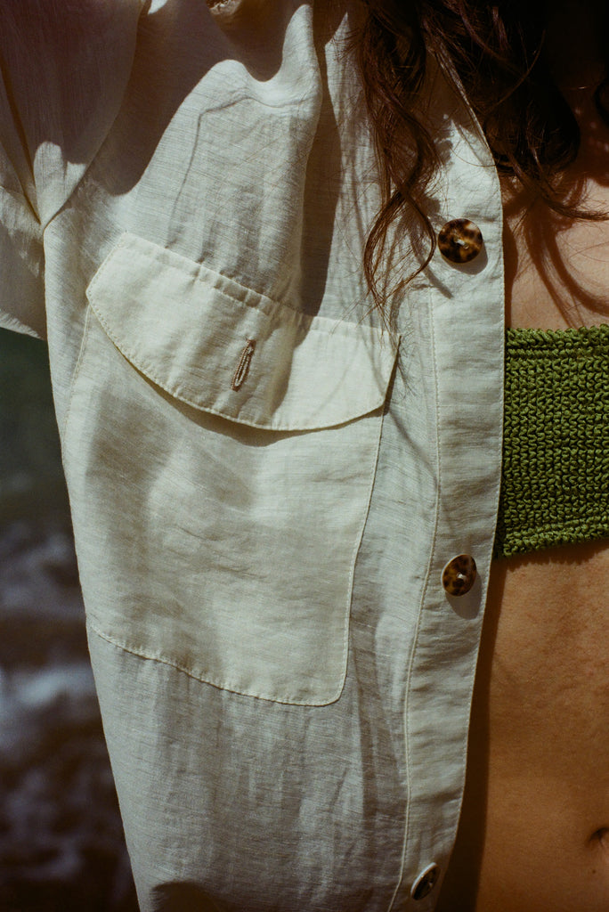 Close up of woman wearing a white button down shirt with pocket and spotted shell buttons.