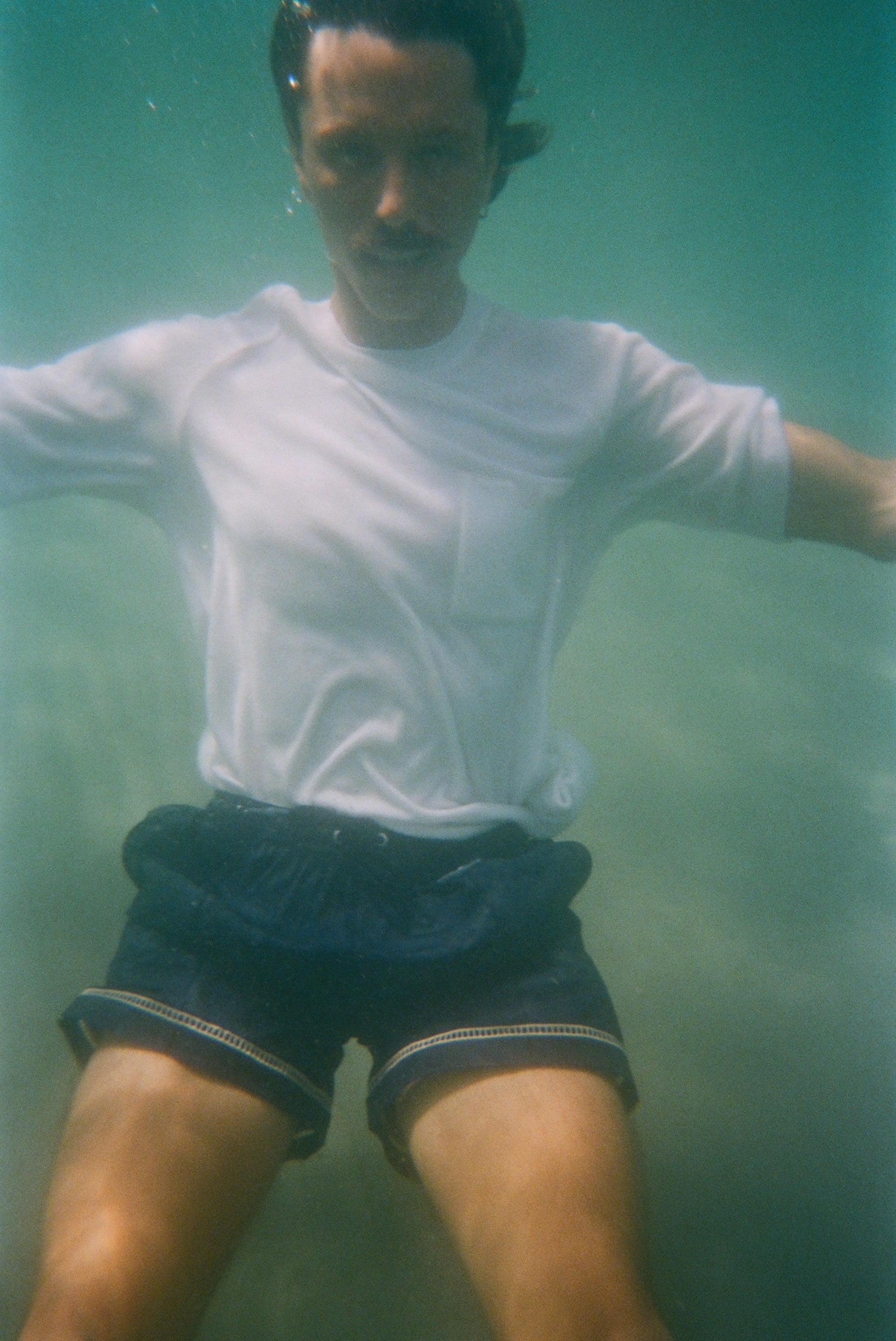Underwater image of male model wearing our white terry t-shirt with navy swim trunks. 