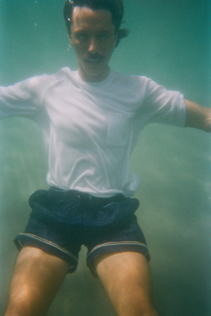 Underwater image of male model wearing our white terry t-shirt with navy swim trunks. 