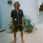 Male model standing and smiling, wearing dark green gambling themed terry cloth cabana, with matching shorts and no shoes. 