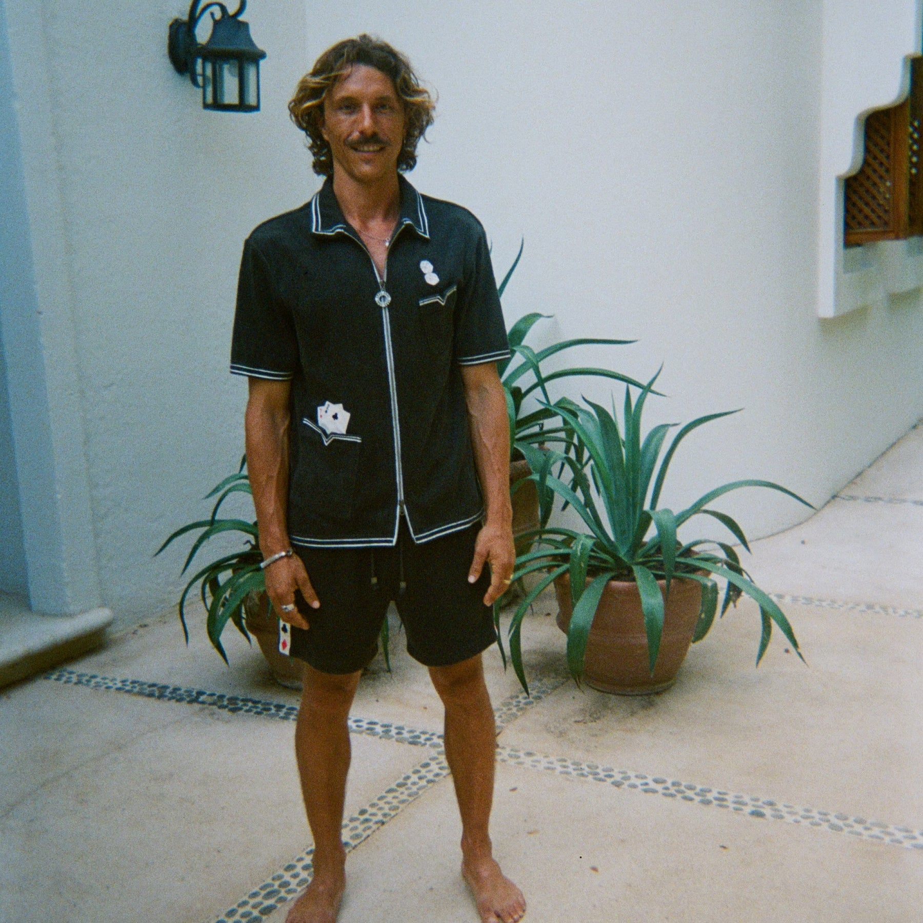 Male model standing and smiling, wearing dark green gambling themed terry cloth cabana, with matching shorts and no shoes. 