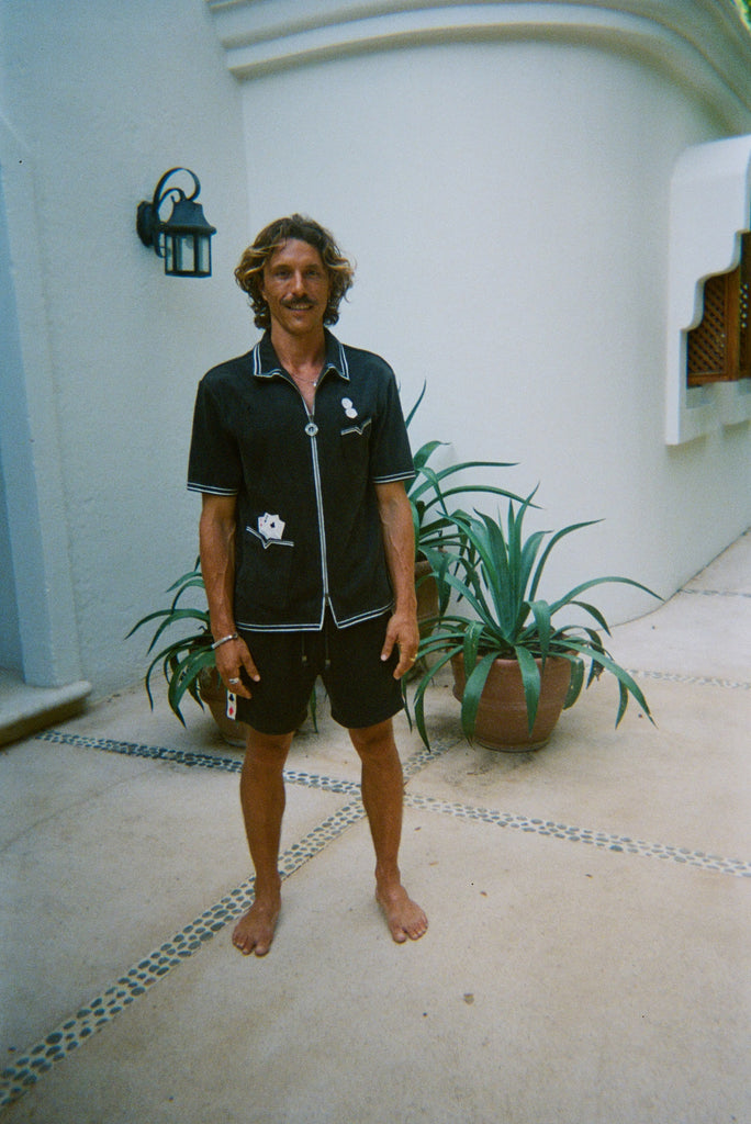Male model standing and smiling, wearing dark green gambling themed terry cloth cabana, with matching shorts and no shoes. 