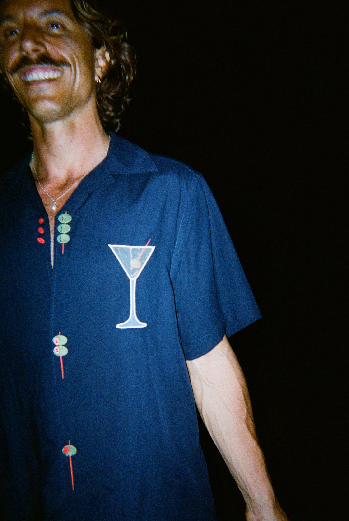 Male model smiling wide wearing the 'Extra Dirty' ~ Relaxed Fit Shirt, featuring a mesh white martini glass over the wearer's left chest. 