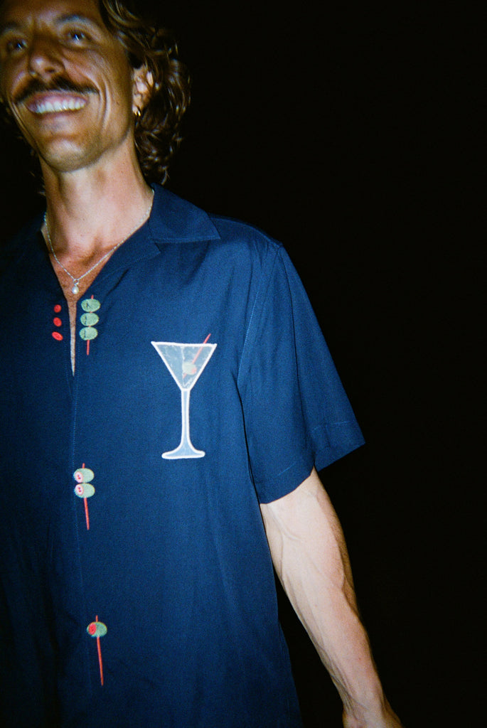 Male model smiling wide wearing the 'Extra Dirty' ~ Relaxed Fit Shirt, featuring a mesh white martini glass over the wearer's left chest. 