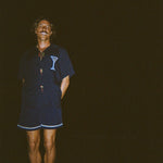 Model smiling widely, standing on the beach at night wearing the 'Extra Dirty' ~ Relaxed Fit Shirt and Navy swim trunks. 