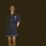 Model smiling widely, standing on the beach at night wearing the 'Extra Dirty' ~ Relaxed Fit Shirt and Navy swim trunks. 