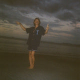 Male model dancing playfully on the beach, wearing the 'Extra Dirty' ~ Relaxed Fit Shirt—a navy short-sleeve button-up with embroidered martini and olive details—and navy swim trunks. The ocean and sand surround him.