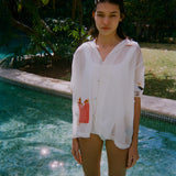 Woman standing in a pool wearing a sheer white short-sleeve shirt with a red gingham pocket embroidered with French fries and a seagull embroidered on the sleeve.