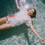  Woman floating in a pool wearing a white button-up shirt with a red gingham pocket embroidered with French fries and a seagull motif on the sleeve.