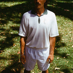 A man wearing a white terry cloth polo shirt with a green collar and matching green accents. He is also wearing white drawstring shorts.