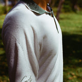 Close-up side view of a man wearing a white terry cloth polo shirt with a green collar and placket. The left sleeve features green script embroidery reading 'Golf' with a dotted line extending upward toward the shoulder. 