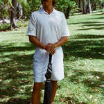 Man in a white polo shirt and shorts holding an umbrella. 