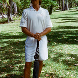 Man in a white polo shirt and shorts holding an umbrella. 