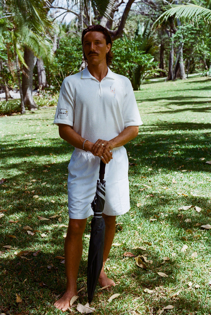 Man in a white polo shirt and shorts holding an umbrella. 