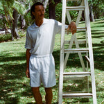 Man wearing a white terry cloth polo with embroidered tennis graphics on the chest and sleeve.