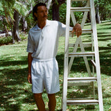 Man wearing a white terry cloth polo with embroidered tennis graphics on the chest and sleeve.