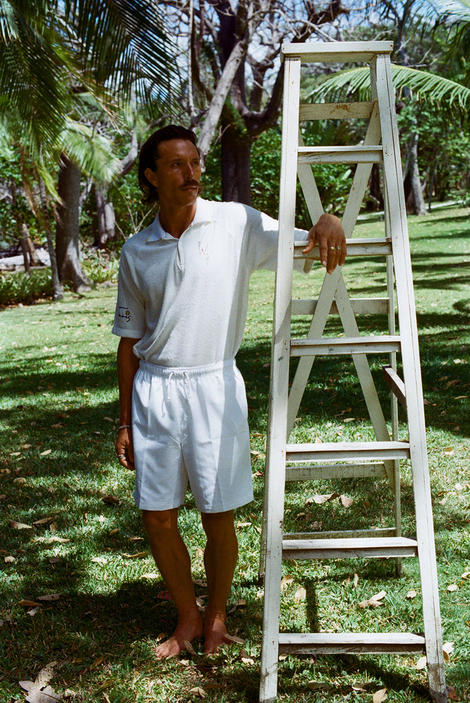 Man wearing a white terry cloth polo with embroidered tennis graphics on the chest and sleeve.