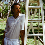 Man wearing a white terry cloth polo with embroidered tennis graphics on the chest and sleeve.