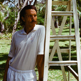 Man wearing a white terry cloth polo with embroidered tennis graphics on the chest and sleeve.
