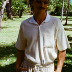 Man posed with hands in pockets, wearing the beige mesh 'TomPolo' and sand linen Easy-Going shorts.