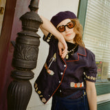Young female model wearing Lesca Lunetier x Tombolo lenses in coral leaning against a pillar wearing a navy beret and Tombolo "Vongole" Cabana in Navy.