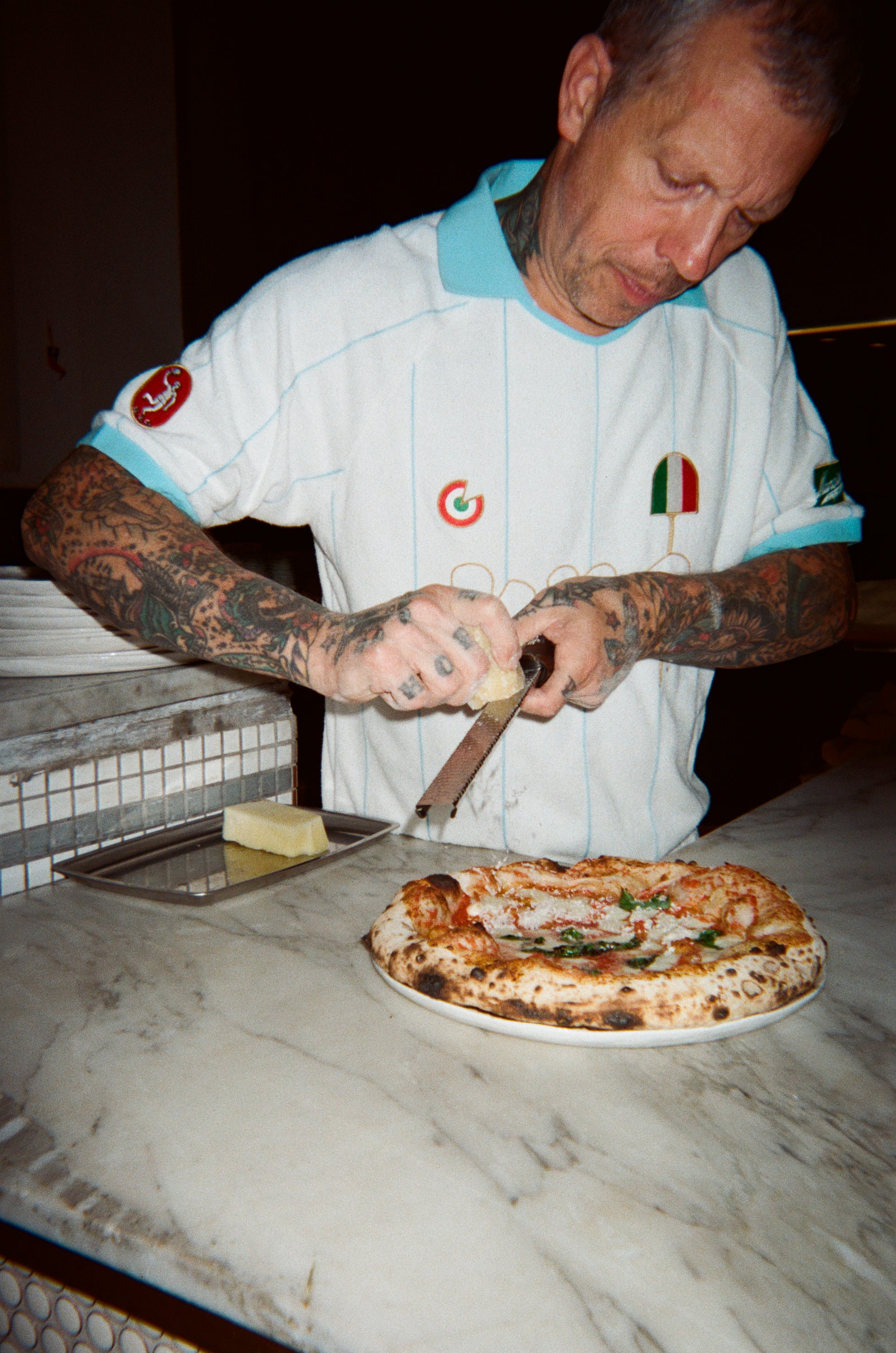 Man grating cheese over a freshly made pizza. 
