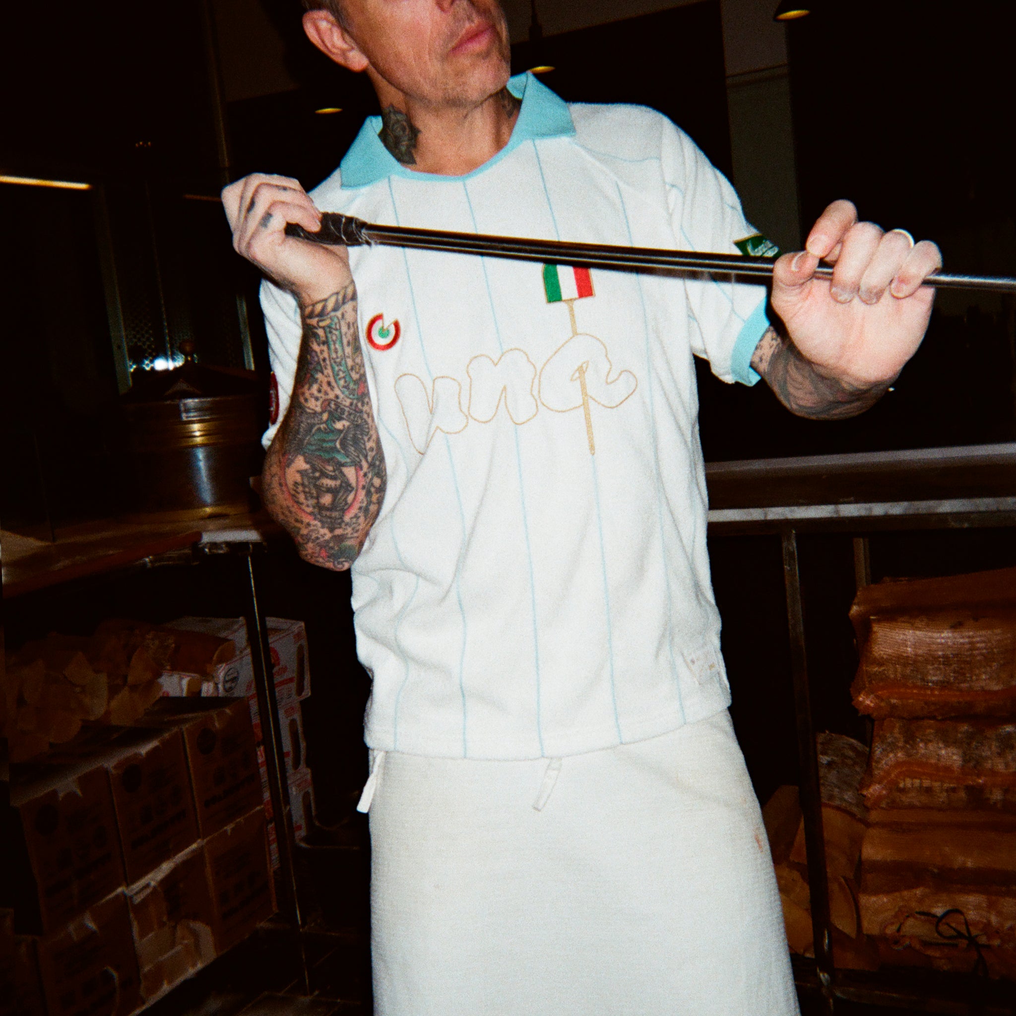 A man wearing a white pizza jersey with a light blue collar and a white apron over it.
